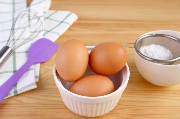 家庭料理のための木製のテーブルの上に泡立て器と台所用品を持つ卵 — ストック写真
