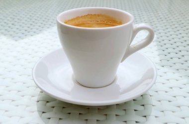 Beyaz masada izole edilmiş bir fincan sıcak köpüklü kahve.