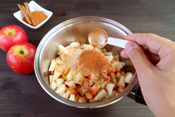 Man\'s hand adding a spoon of ground cinnamon into the pot of diced apples for making apple compote