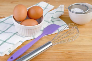 Tahta masa üzerinde yumurta ve mutfak aletleriyle çırpılmış bir spatula.