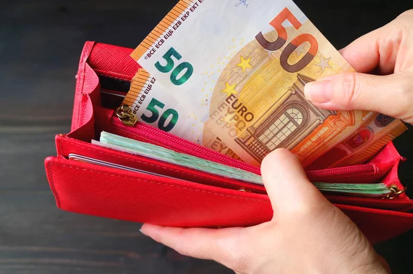 Kırmızı bir cüzdanda bir avuç Euro banknotunu tutan bir kadının resmi.
