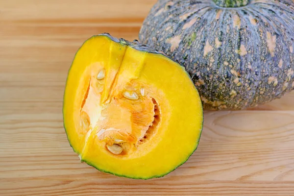 Piece of Cut Fresh Pumpkin with a Whole Fruit Isolated on Light Wooden Table