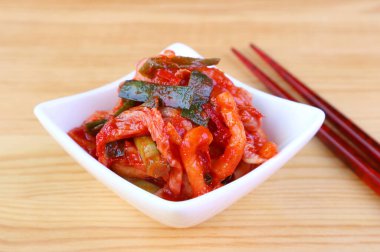 Bir kase Iconic Kore Dish Kimchi, üzerinde bir çift yemek çubuğu olan tahta masa.