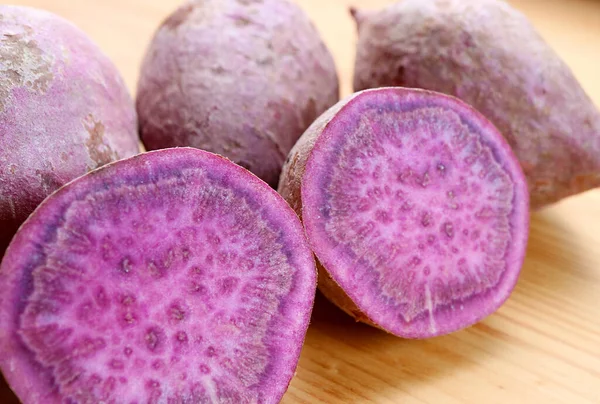 Closeup of Cross-section of Raw Purple Sweet Potatoes with Blurry Whole Roots in Backdrop