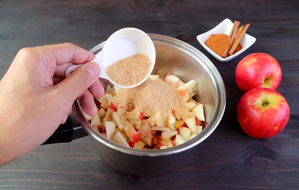 Hand adding unrefined sugar into the pot of diced apples for making a healthy compote