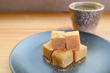 Plate of Warabimochi, a Japanese Traditional Confection with Blurry Hot Matcha Green Tea in Backdrop