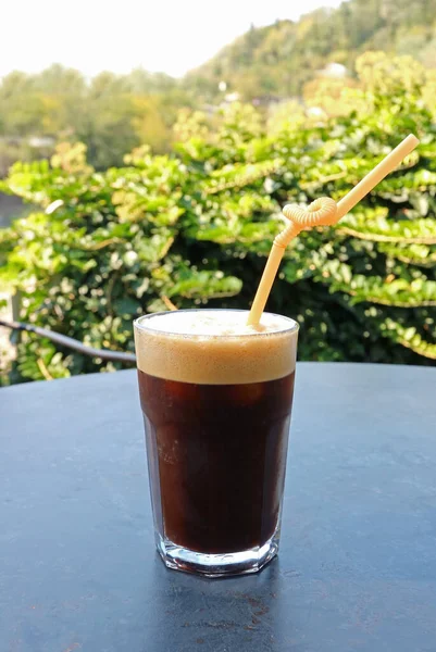 A Glass of Iced Frothy Coffee Isolated on Garden Table