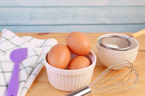 Eggs, whisk and kitchen tools on wooden table for the concept of COOKING