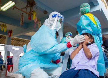 CHIANG MAI, THAILAND - Ban Pamuad Okulu 'nda hızlı bir antijen testi için bir sağlık çalışanı bir öğrenciden burun örneği alır. Tayland 5-11 yaşlarındaki çocukları aşılamaya başladı..