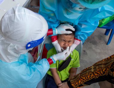 CHIANG MAI, THAILAND - Ban Pamuad Okulu 'nda hızlı bir antijen testi için bir sağlık çalışanı bir öğrenciden burun örneği alır. Tayland 5-11 yaşlarındaki çocukları aşılamaya başladı..