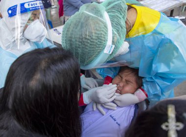 CHIANG MAI, THAILAND - Ban Pamuad Okulu 'nda hızlı bir antijen testi için bir sağlık çalışanı bir öğrenciden burun örneği alır. Tayland 5-11 yaşlarındaki çocukları aşılamaya başladı..