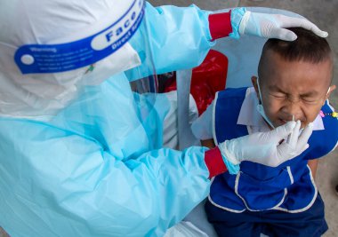 CHIANG MAI, THAILAND - Ban Pamuad Okulu 'nda hızlı bir antijen testi için bir sağlık çalışanı bir öğrenciden burun örneği alır. Tayland 5-11 yaşlarındaki çocukları aşılamaya başladı..