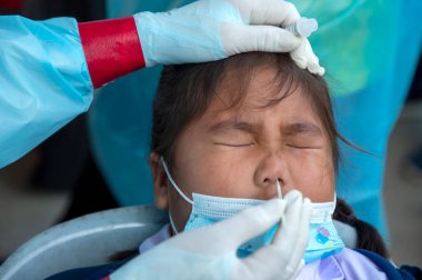 CHIANG MAI, THAILAND - Ban Pamuad Okulu 'nda hızlı bir antijen testi için bir sağlık çalışanı bir öğrenciden burun örneği alır. Tayland 5-11 yaşlarındaki çocukları aşılamaya başladı..