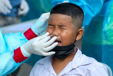 CHIANG MAI, THAILAND - Ban Pamuad Okulu 'nda hızlı bir antijen testi için bir sağlık çalışanı bir öğrenciden burun örneği alır. Tayland 5-11 yaşlarındaki çocukları aşılamaya başladı..
