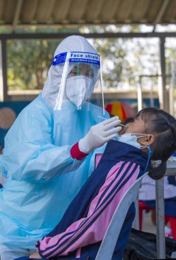 CHIANG MAI, THAILAND - Ban Pamuad Okulu 'nda hızlı bir antijen testi için bir sağlık çalışanı bir öğrenciden burun örneği alır. Tayland 5-11 yaşlarındaki çocukları aşılamaya başladı..