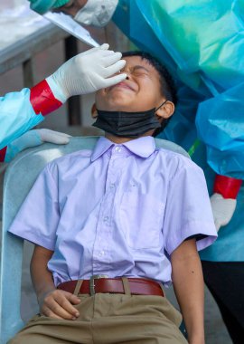 CHIANG MAI, THAILAND - Ban Pamuad Okulu 'nda hızlı bir antijen testi için bir sağlık çalışanı bir öğrenciden burun örneği alır. Tayland 5-11 yaşlarındaki çocukları aşılamaya başladı..