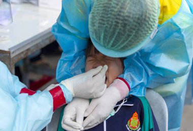 CHIANG MAI, THAILAND - Ban Pamuad Okulu 'nda hızlı bir antijen testi için bir sağlık çalışanı bir öğrenciden burun örneği alır. Tayland 5-11 yaşlarındaki çocukları aşılamaya başladı.. 
