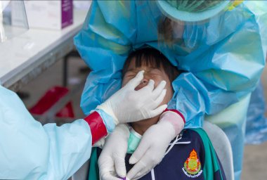 CHIANG MAI, THAILAND - Ban Pamuad Okulu 'nda hızlı bir antijen testi için bir sağlık çalışanı bir öğrenciden burun örneği alır. Tayland 5-11 yaşlarındaki çocukları aşılamaya başladı.. 