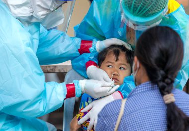 CHIANG MAI, THAILAND - Ban Pamuad Okulu 'nda hızlı bir antijen testi için bir sağlık çalışanı bir öğrenciden burun örneği alır. Tayland 5-11 yaşlarındaki çocukları aşılamaya başladı.. 