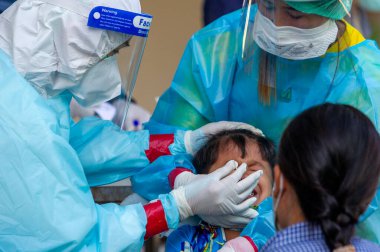 CHIANG MAI, THAILAND - Ban Pamuad Okulu 'nda hızlı bir antijen testi için bir sağlık çalışanı bir öğrenciden burun örneği alır. Tayland 5-11 yaşlarındaki çocukları aşılamaya başladı.. 