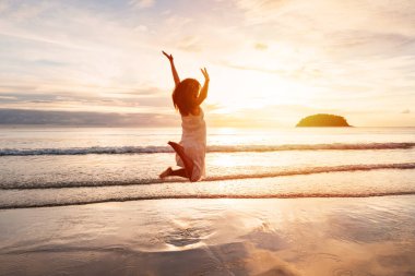 Young woman traveler jumping and enjoying beautiful Sunset on the tranquil beach, Travel on summer vacation concept