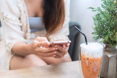 İçki içen genç bir kadın cep telefonu kullanıyor ve kafede dinleniyor, modern yaşam tarzı.