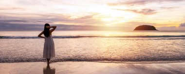 Young female relaxing and looking beautiful sunset over the sea as a tranquil tropical beach and waves for summer vacation