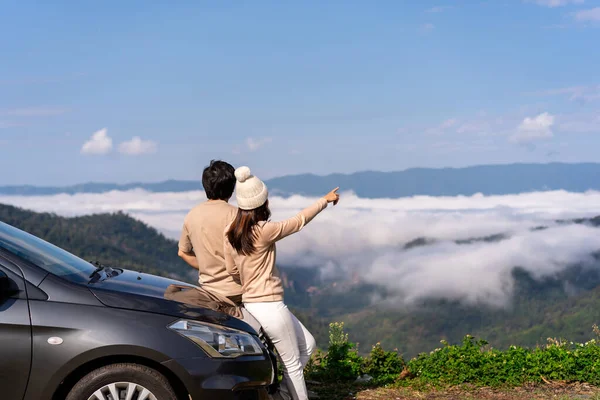 Young couple travelers with car watching a beautiful sea of fog over the mountain while travel driving road trip on vacation