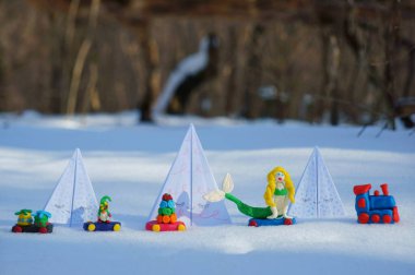Karlı bir ormanda kağıt oyuncak Noel ağaçları. Yanındaki oyuncak tren plastikten yapılma..