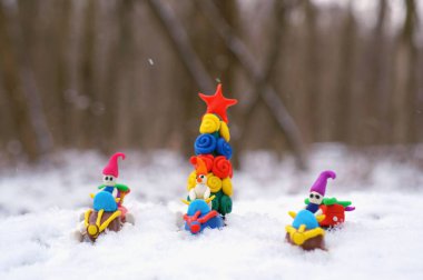 Plastikten yapılmış bir kar aracındaki Noel figürleri Noel ağacı ve hediyeler taşıyor. Eylem, karlı bir ormanda gerçekleşiyor..