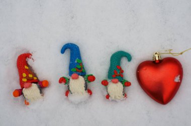 Karlı bir ormanda çok renkli cücelerin figürleri. Yakınlarda oyuncak bir kalp var..