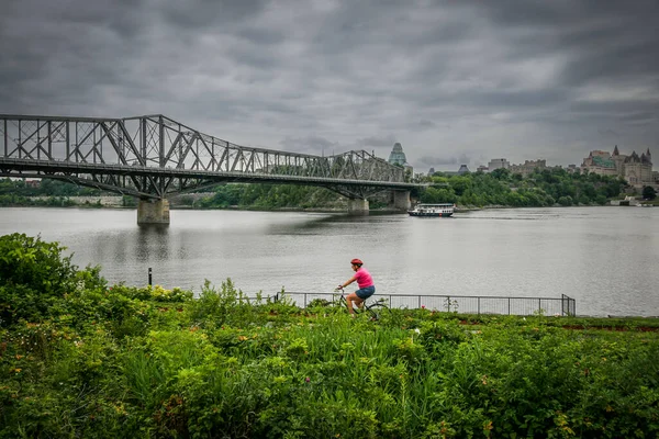 Αλεξάνδρα γέφυρα σε όλη την Οττάβα ποταμού με έναν ποδηλάτη ιππασία κατά μήκος της όχθης — Φωτογραφία Αρχείου