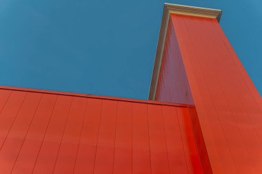 Açık mavi gökyüzüne karşı binanın canlı kırmızı üst kısmı soyut bir şekil oluşturuyor.