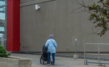 Toronto, Kanada, Ağustos 2021 - Mavi gömlekli ve kot pantolonlu bir kadın bir binanın yanında bebek arabasıyla yürüyor