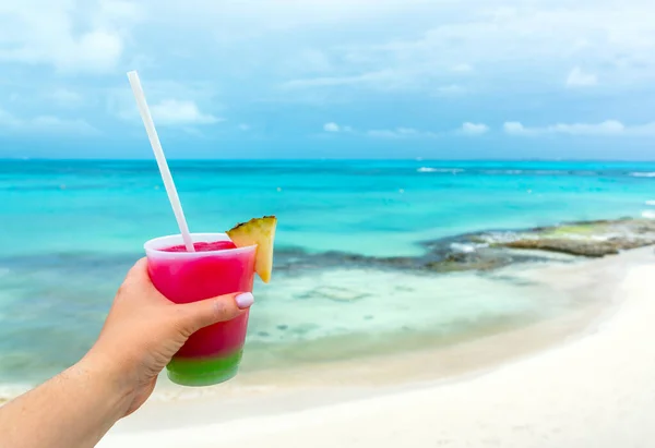 Persoonlijk perspectief op Vrouwelijke hand die glas vasthoudt en cocktails drinkt aan de Caribische zee. Blauwe oceaan op de achtergrond. Vakantie in de tropen. — Stockfoto