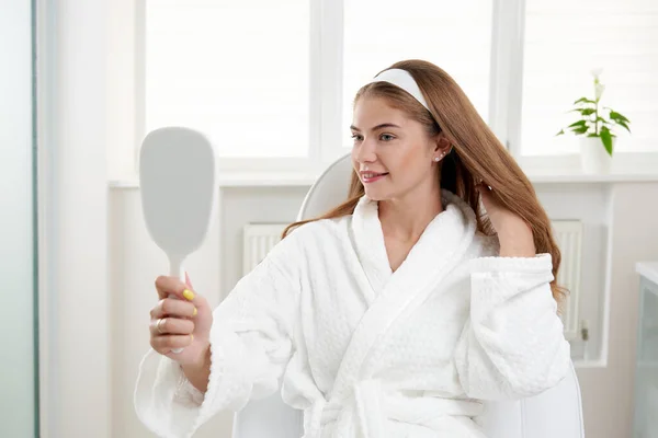 Mujer en el salón de cosmetología satisfecho con el resultado del procedimiento cosmético. Mujer mirando el espejo y examinando la piel — Foto de Stock