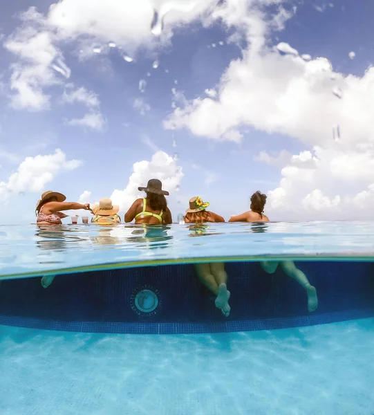 Half underwater split image of young women having fun in hotel pool in Caribbean sea. Concept of vacation and bachelorette pool party