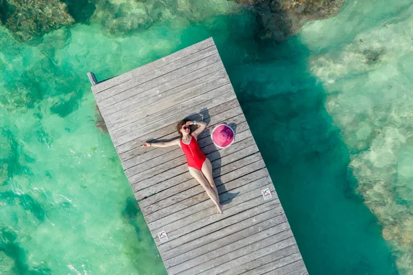 Luftaufnahme einer Frau, die an einem sonnigen Sommertag in Cancun, Mexiko, auf einem Holzsteg liegt, von oben. Junge sexy Frau im roten Badeanzug im Sommer in der Karibik. Sommerferienkonzept — Stockfoto