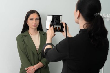 Doktor, beyaz arka planda estetik tedaviden önce üç boyutlu kamera sistemiyle kadın hastanın fotoğrafını çekiyor.