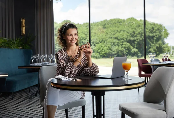 Schöne junge lockige Frau sitzt in einem Café und trinkt frischen Orangensaft und wartet auf ihren Freund — Stockfoto
