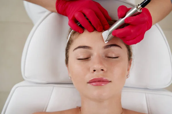 Kosmetolog czyszczący sprzętowo twarz pięknej młodej pacjentki. Koncepcja oczyszczania i przywracania elastyczności skóry — Zdjęcie stockowe