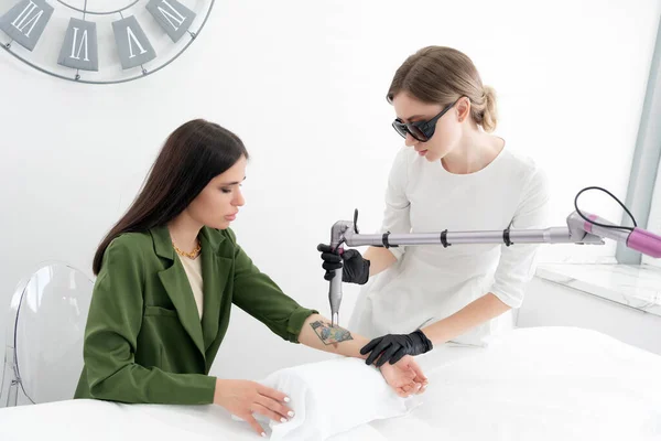 Esteticista usando dispositivo laser para remover uma tatuagem indesejada do braço feminino. Conceito de apagar tatuagens como um procedimento caro em uma clínica de cosmetologia — Fotografia de Stock