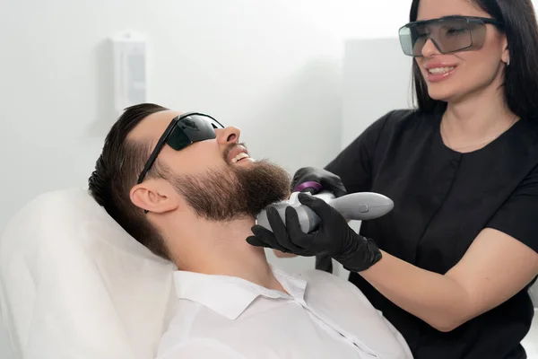 Młody brodaty mężczyzna leczony laserowo przez profesjonalnego kosmetologa w klinice kosmetycznej. Koncepcja zdrowego stylu życia człowieka — Zdjęcie stockowe