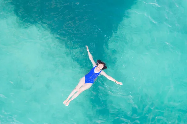 Luftaufnahme einer Frau in blauem Badeanzug, die auf einer transparenten türkisfarbenen Wasseroberfläche am karibischen Strand liegt. Reise- und Urlaubskonzept. Tropischer Hintergrund mit Kopierraum — Stockfoto