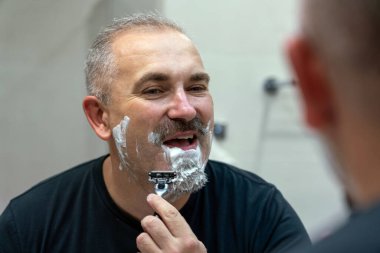 Orta yaşlı yakışıklı adam banyoda sakalını kesiyor.