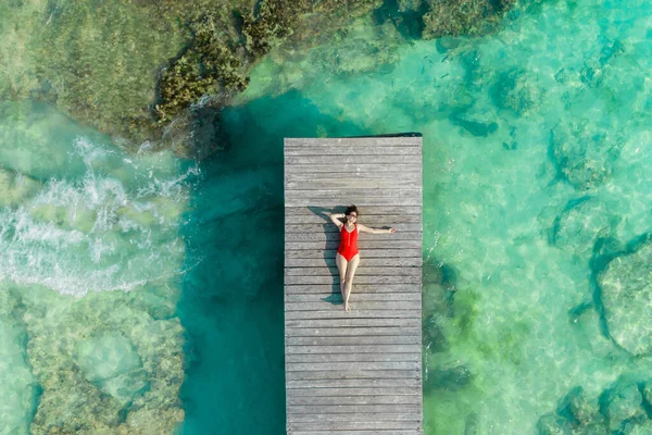 Luftaufnahme einer Frau, die an einem sonnigen Sommertag in Cancun, Mexiko, auf einem Holzsteg liegt, von oben. Junge sexy Frau in hellem Badeanzug im Sommer in der Karibik. Sommerferienkonzept — Stockfoto
