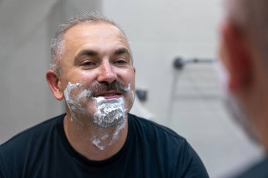 Orta yaşlı yakışıklı adam banyoda sakalını kesiyor.