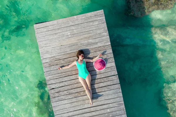 Luchtfoto van vrouw liggend op houten pier op zonnige zomerdag in Cancun, Mexico, bovenaanzicht. Jonge sexy vrouw draagt een helder zwempak in de zomer in het Caribisch gebied. Zomer strand vakantie concept — Stockfoto
