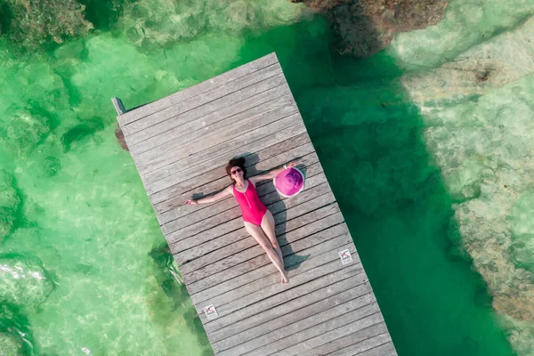 Luftaufnahme einer Frau, die an einem sonnigen Sommertag in Cancun, Mexiko, auf einem Holzsteg liegt, von oben. Junge sexy Frau in hellem Badeanzug im Sommer in der Karibik. Sommerferienkonzept — Stockfoto