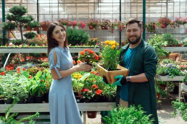 Worker helping female customer to buy flowers in garden center
